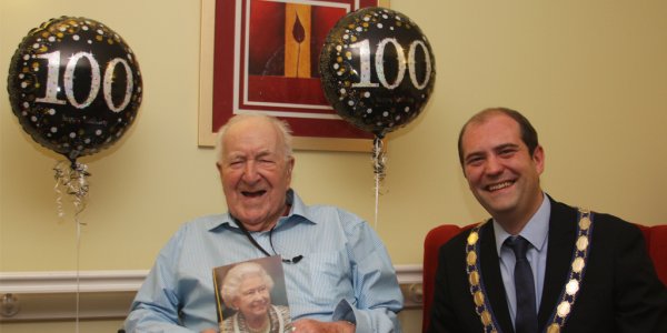 Maurice holding a birthday card from the Queen, sitting with Town Mayor Councillor Walsh