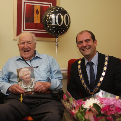 Maurice holding a birthday card from the Queen, sitting with Town Mayor Councillor Walsh